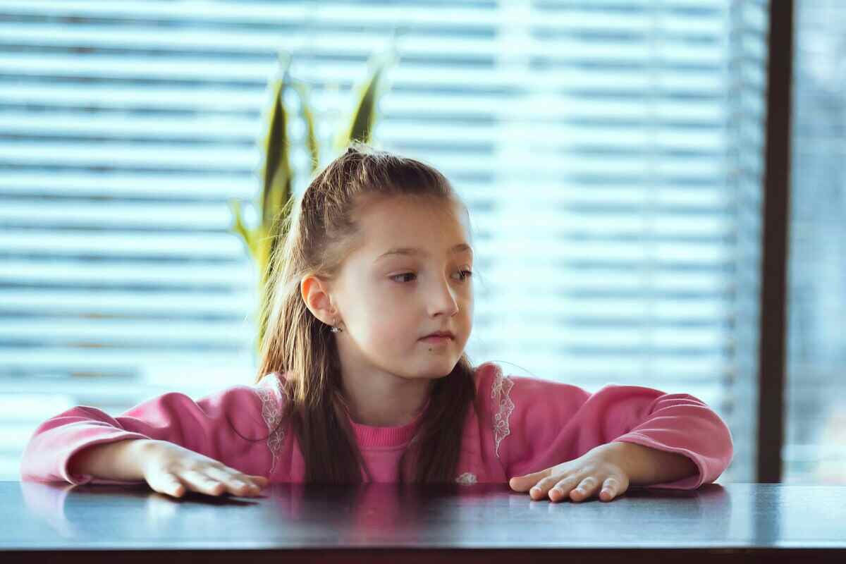 bambina appoggiata al tavolo con le mani da sola